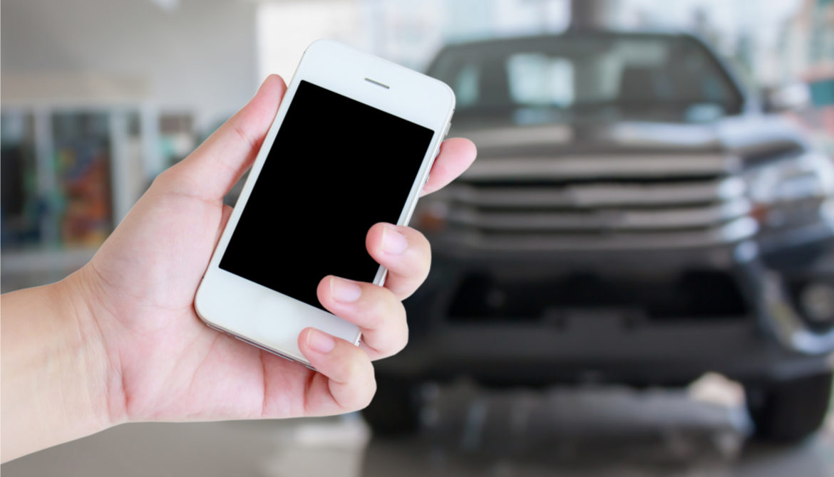 Smartphone with car dealership blurred in background