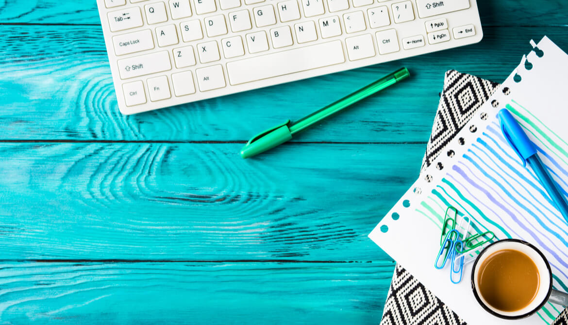 Pens and notebook next to a keyboard on a green wooden desktop