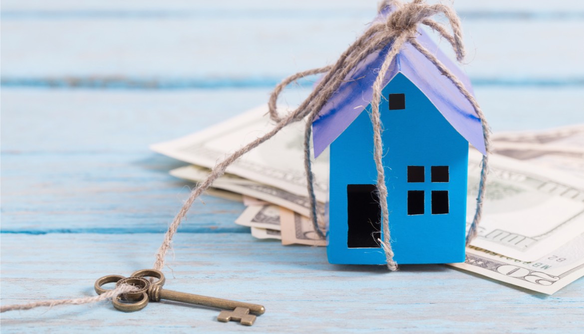 blue paper house tied to an old fashioned key sitting on a stack of US dollars