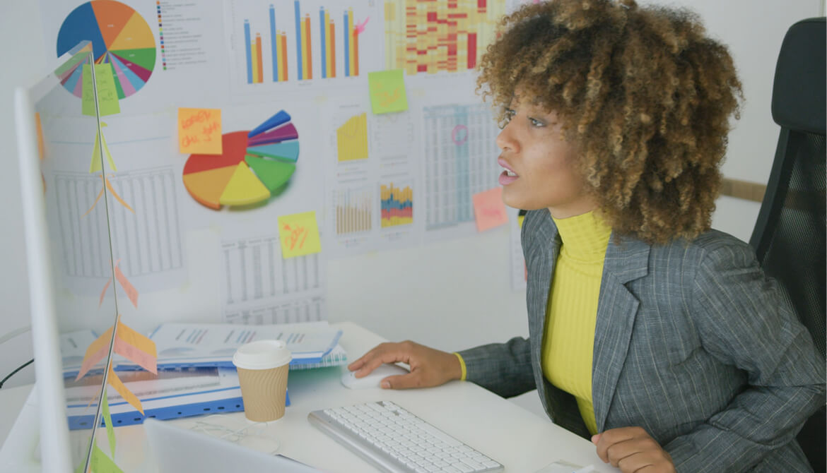 Woman sitting at working desktop with charts on wall and doing her job on computer looking serious