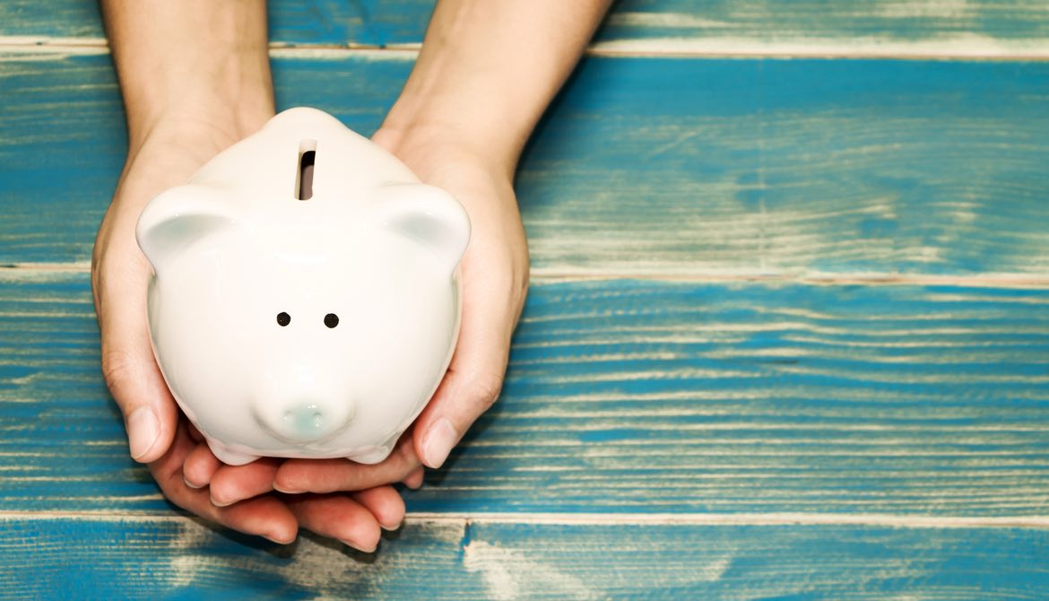 hands holding white piggy bank on a blue wood table