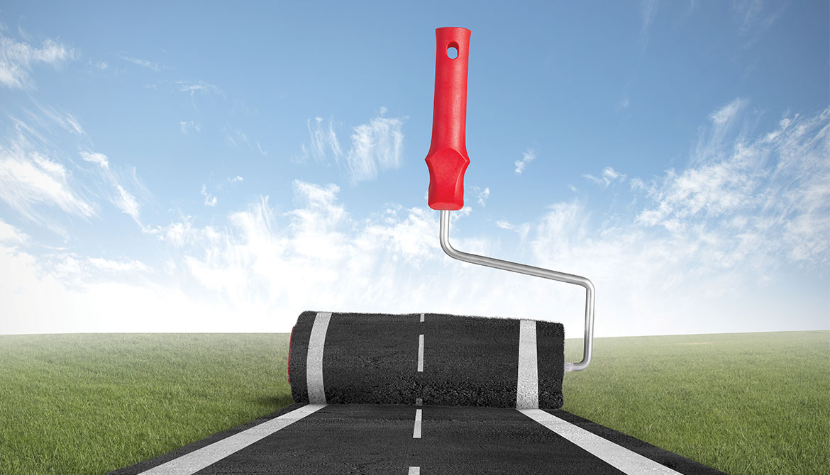 giant paint roller applying road pavement to landscape