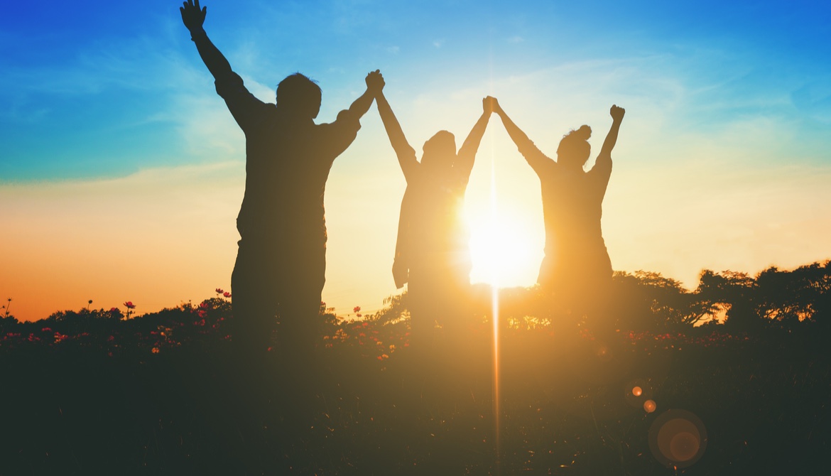 three people with their arms up to the sky with the glow of the sun