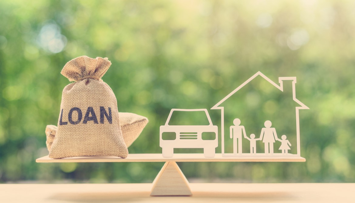 burlap bag with loan written on it balancing with a car and house on a wooden balance