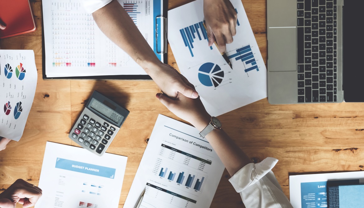 overhead shot of handshake over a table with financial charts