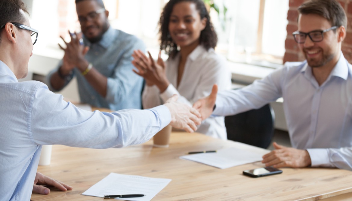 business professionals shaking hands in agreement while team applauds