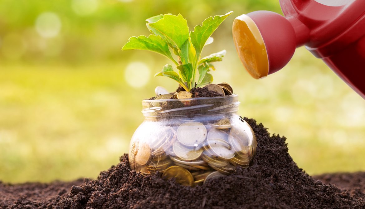 red watering can with jar of money stuck in soil and a plant growing out of it