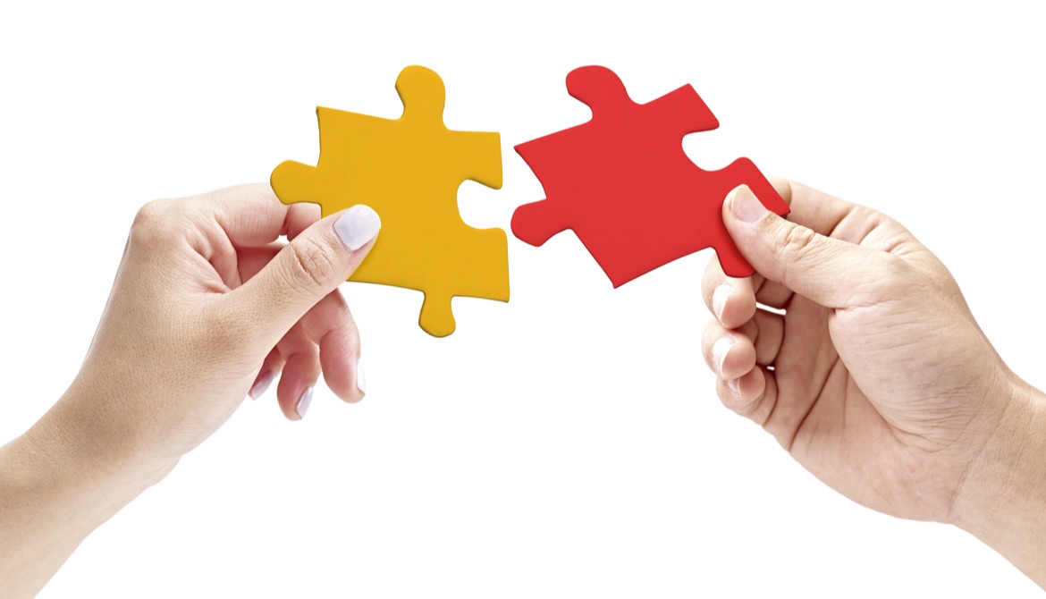 two hands putting together a red and a yellow puzzle piece