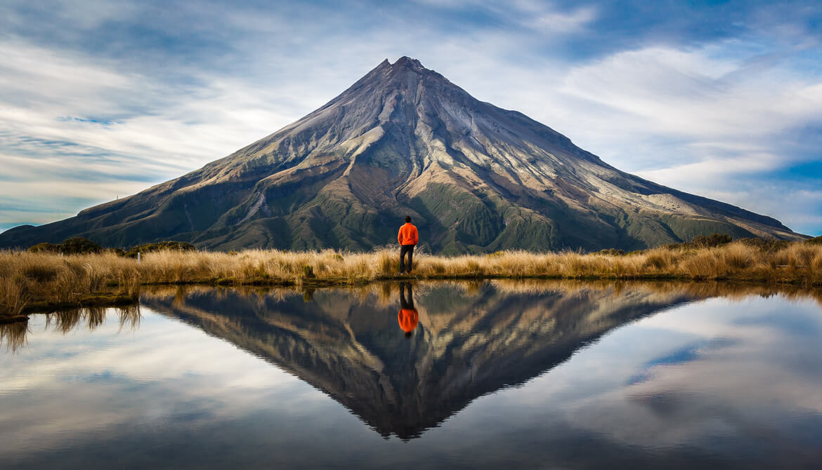 mountaineer looking at mountain with reflection of mountain behind in lake