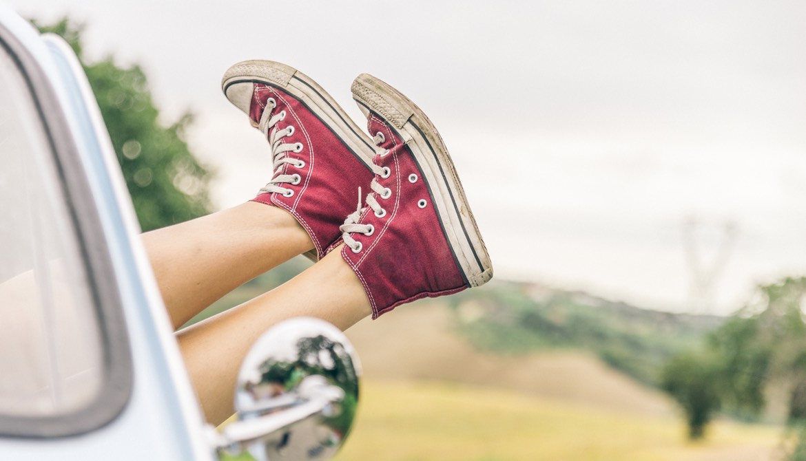 woman hanging feet in red sneakers out window of car