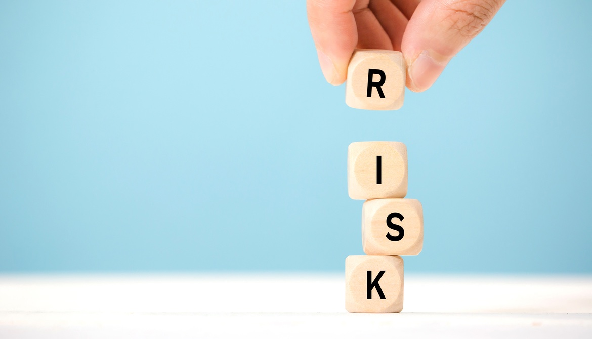 hand carefully placing R block on top of tower of letter blocks to complete the word RISK