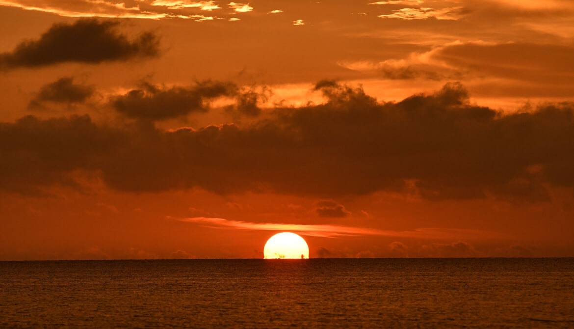 sun sinks below ocean horizon on cloudy evening