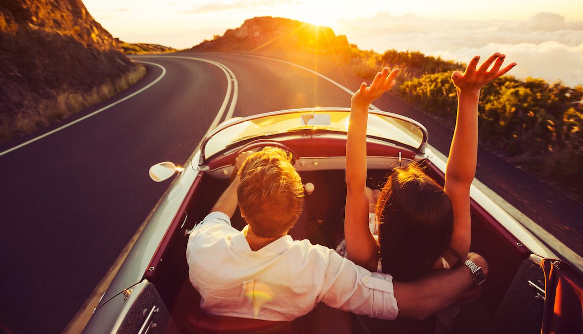 raised arms while driving car at sunset