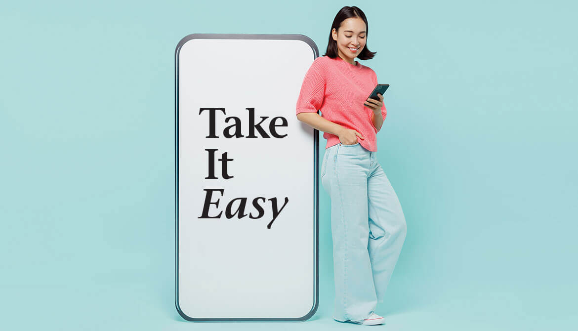 young woman in pink sweater using smartphone while standing next to a giant smartphone screen