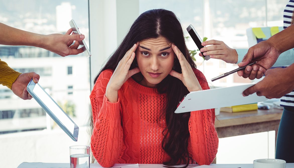 young business woman holds head as colleagues in the office hand her more and more work