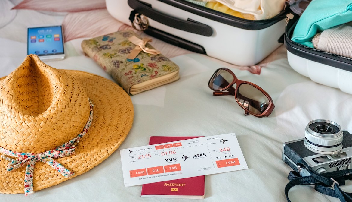 straw summer hat with plane ticket phone and camera next to open luggage