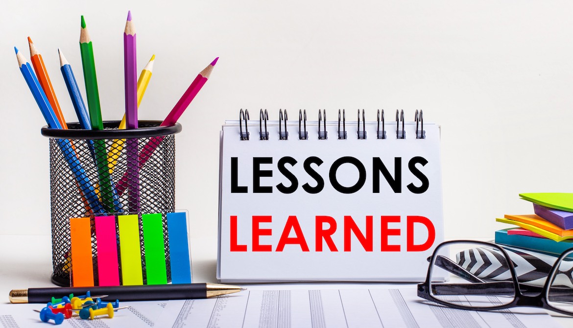 glasses and colored pencils with office supplies in front of notebook that reads LESSONS LEARNED