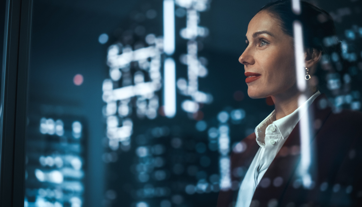 a successful businesswoman looks out at the lit up city skyline