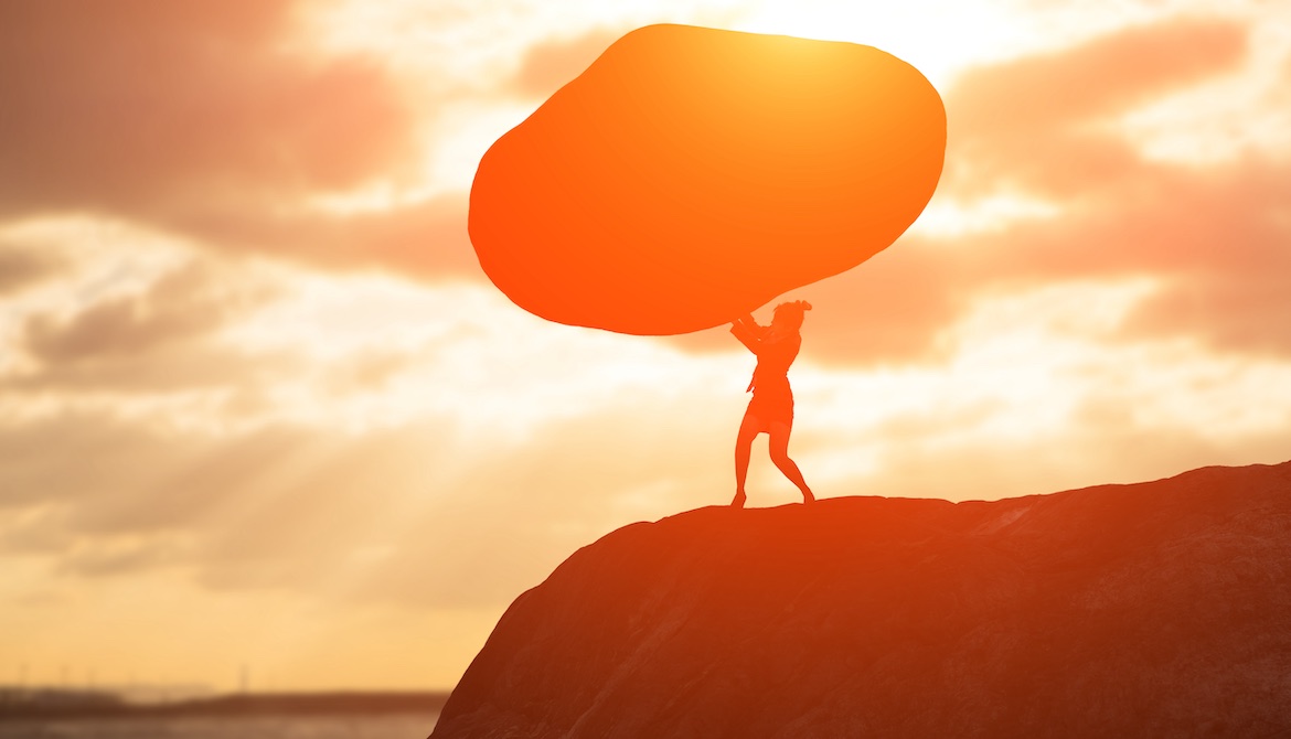 ambitious woman pushing up large boulder while standing on rocky outcrop