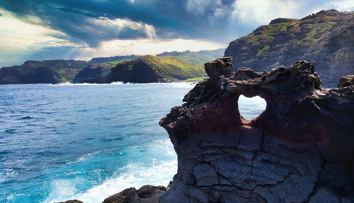 A hole in rocks in Maui forms a heart with ocean in background