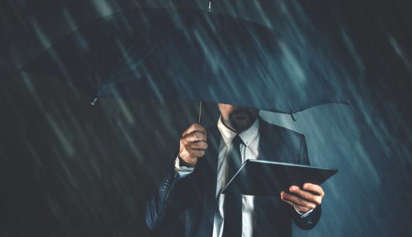 business man holds tablet under an umbrella on a dark rainy day