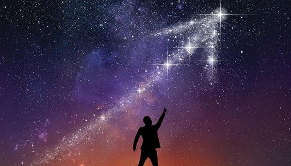 silhouette of a person pointing up at a galaxy in the shape of an upward arrow in the night sky