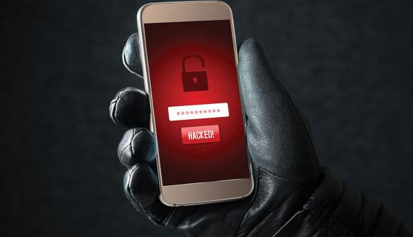 black leather gloved hand holds up smartphone with red screen depicting an open padlock and the word hacked