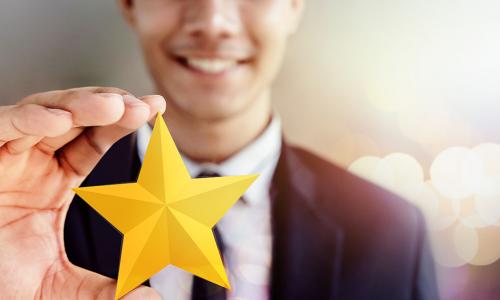 Happy Businessman in black suit Smiling and Showing a Golden Star in Hand