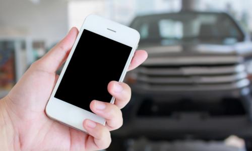 Smartphone with car dealership blurred in background