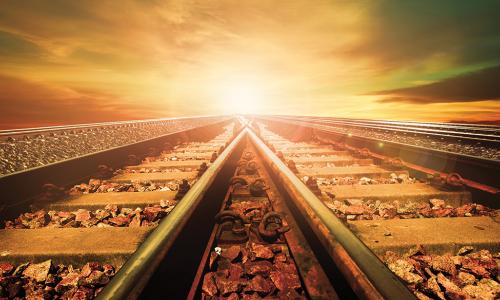 train tracks converging in front of a sunset sky