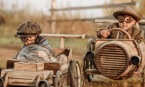 Two boys in helmets and goggles racing in wooden toy cars