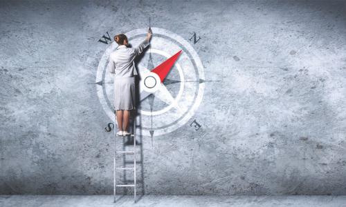 a woman on a ladder draws a compass on a gray wall