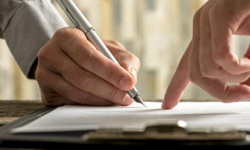 hand pointing to a contract that another businessman is about to sign