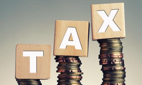 tax spelled out in wooden blocks on stacks of coins