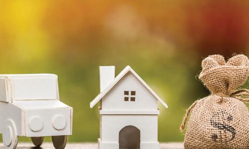 wooden models of a car and house next to a burlap money bag