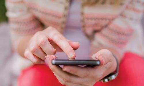 Colorfully dressed young woman leaning forward to use smartphone