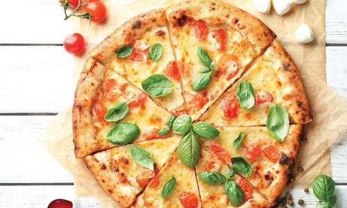 sliced margherita pizza with fresh basil on a white wooden table