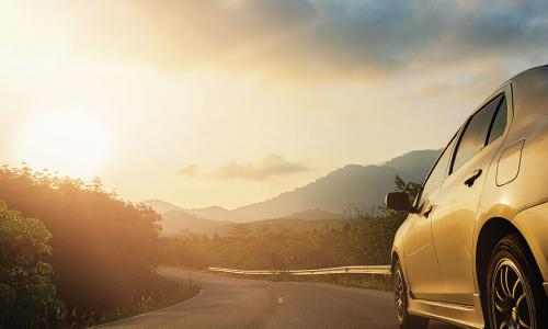 car driving along rough winding road toward distant hills at sunrise