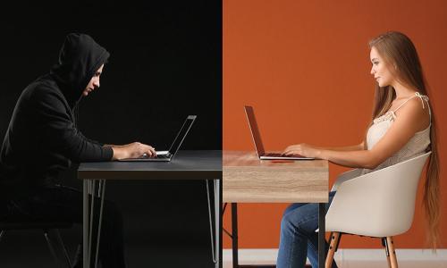 young woman working on laptop across table from a hacker wearing a dark hoodie