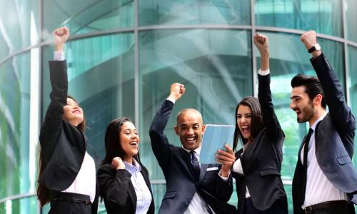 team of cheering colleagues gathered around a coworker holding a digital tablet