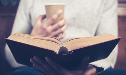 young leader reading a red hardcover book while holding a paper coffee cup