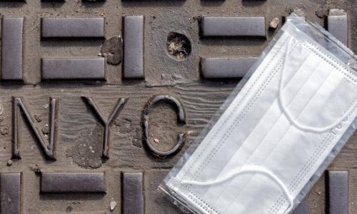 surgical mask on the ground by an NYC stamped in metal