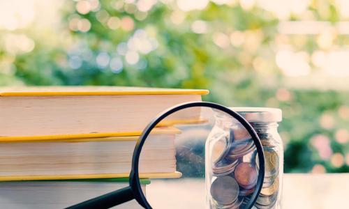 books with nearby money zoomed by a magnifying glass