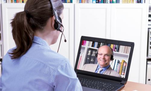 woman sitting with laptop meeting with executive on screen