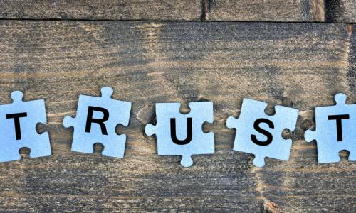 Letters of word TRUST spelled on blue puzzle pieces on wooden table