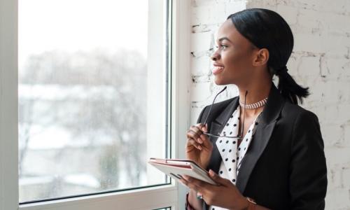 happy introverted businesswoman works alone on tablet while looking out window