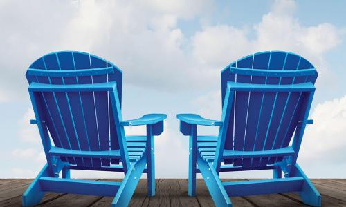 pair of blue Adirondack chairs on wooden deck facing blue sky