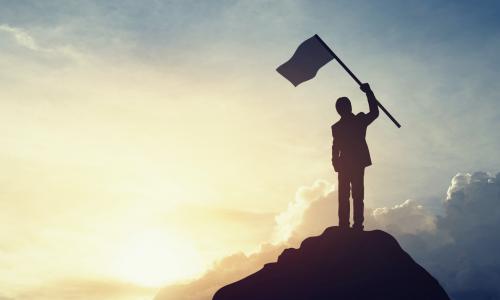 Silhouette of businessman hold a flag on top mountain sky and sun light background