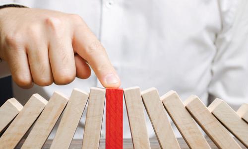 businessman reaches out finger to stop red wooden block from falling while propping up the fallen wooden blocks around it 