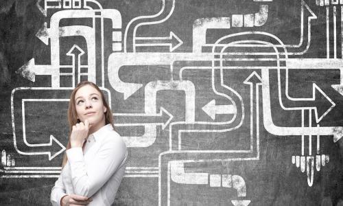 young female leader thinking strategically in front of chalkboard with drawings of many bending arrows